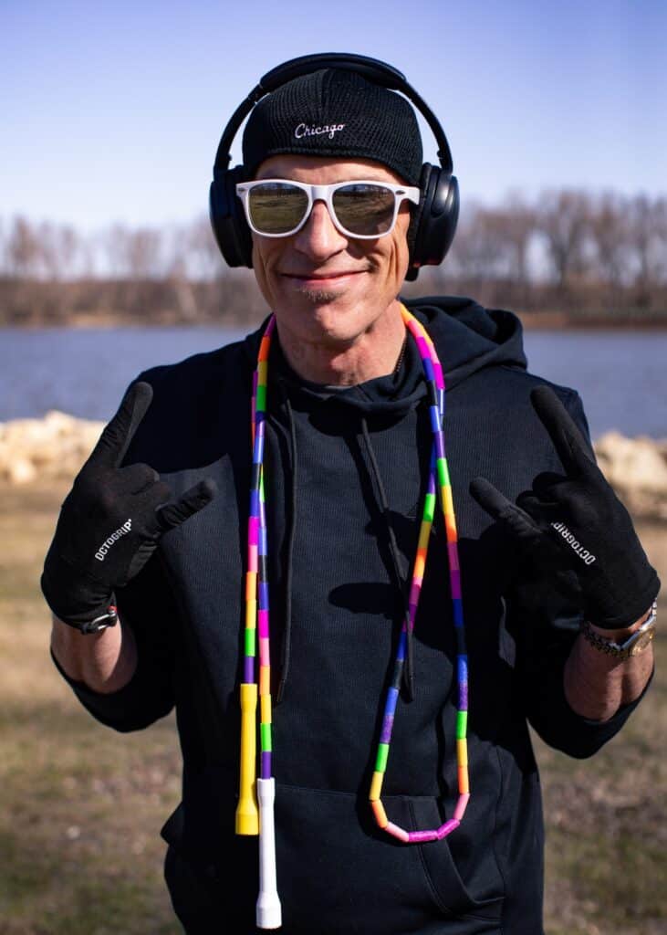 Dizzy Skips smiling and throwing the horns with a jump rope, hat, sunglasses, and headphones